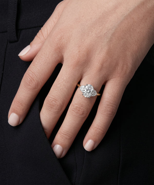 Three-stone oval diamond ring with a yellow gold band on a model's hand.