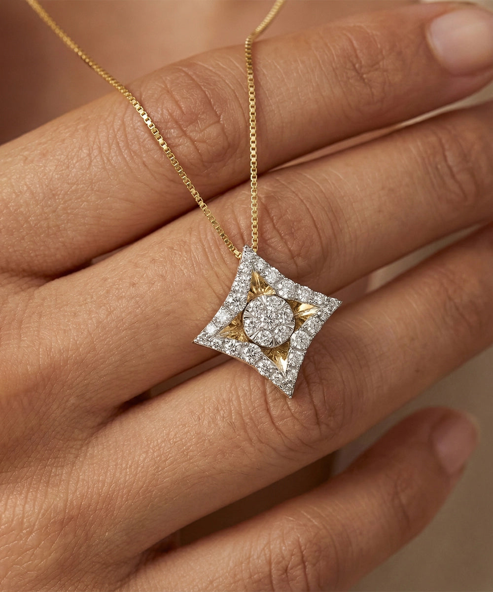 Gold necklace with a diamond pendant held by a hand against a neutral background