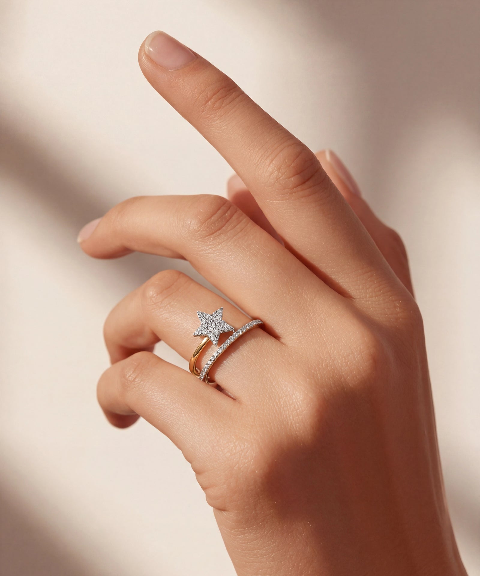 Hand wearing two diamond rings on a neutral background