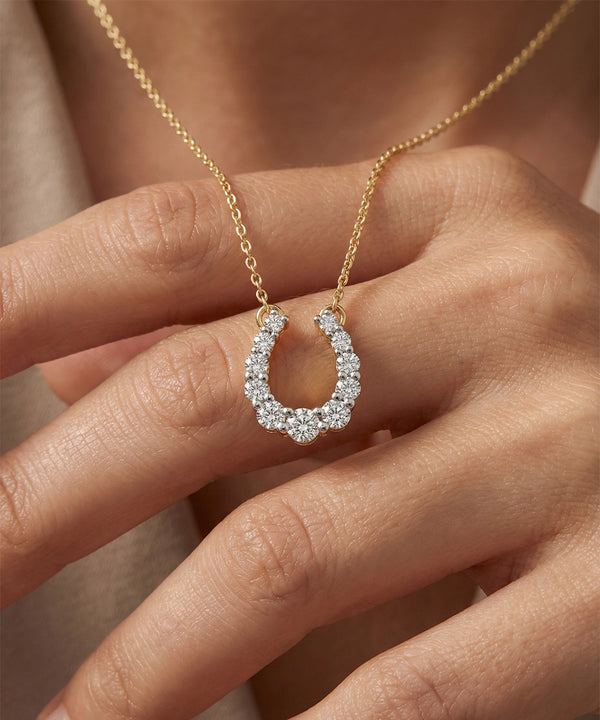 Gold necklace with a diamond horseshoe pendant held by a hand.