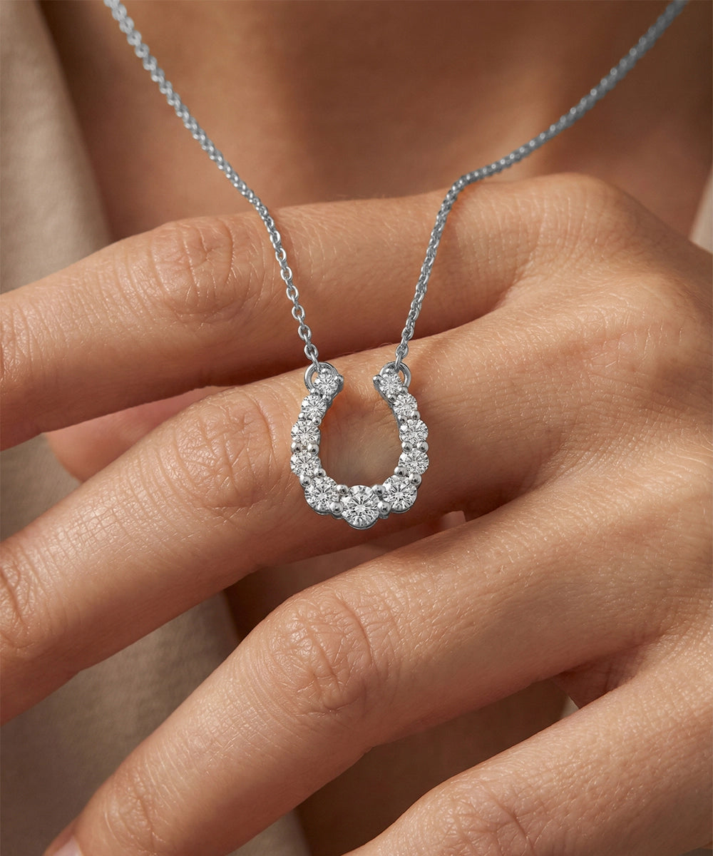 Silver necklace with a horse shoe-shaped pendant held by a hand