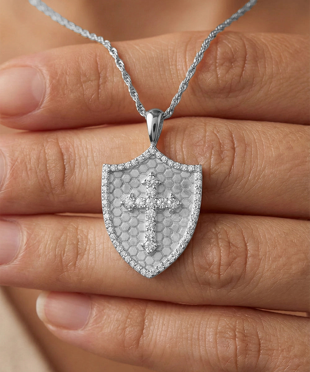 Silver shield-shaped pendant with a cross on a hand