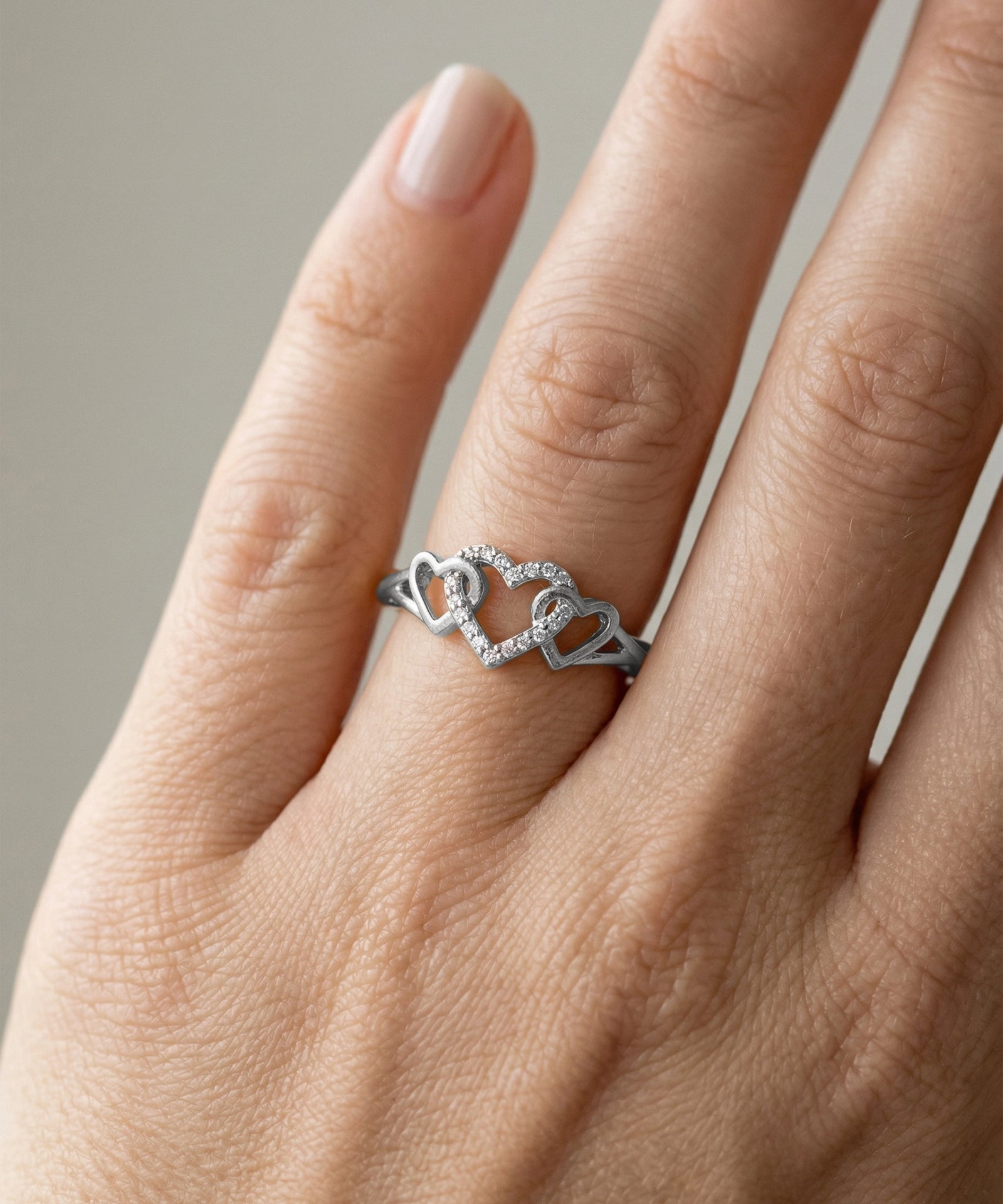 Silver ring with heart design on a person's finger against a neutral background