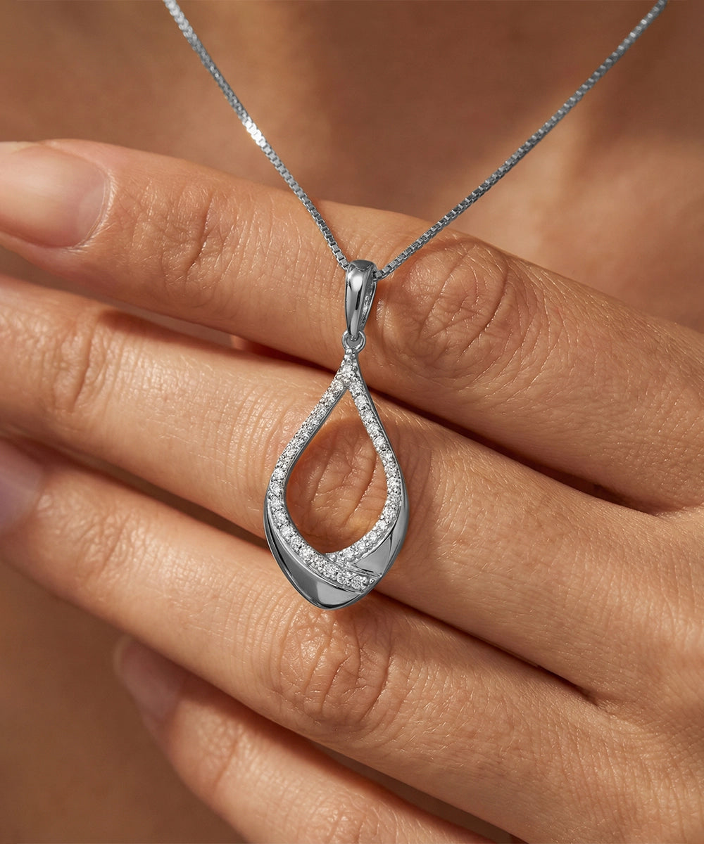 Silver teardrop pendant on a chain held between fingers