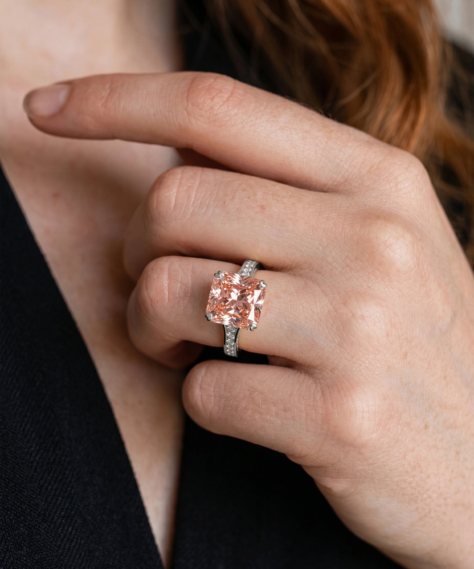 Hand wearing a ring with a pink gemstone against a neutral background