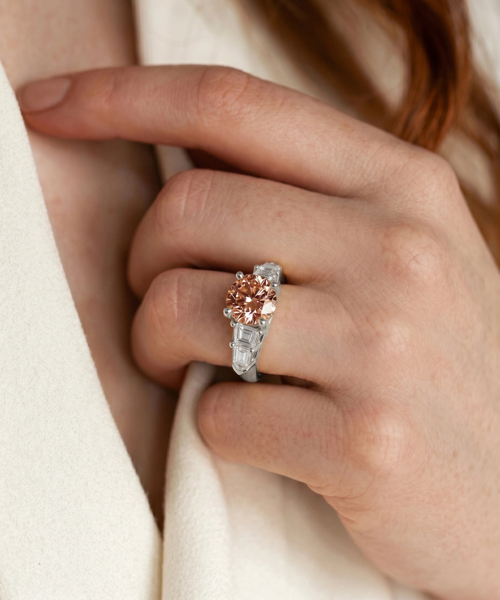 Close-up of a hand wearing a ring with a central brown gemstone and smaller clear stones, against a neutral background.