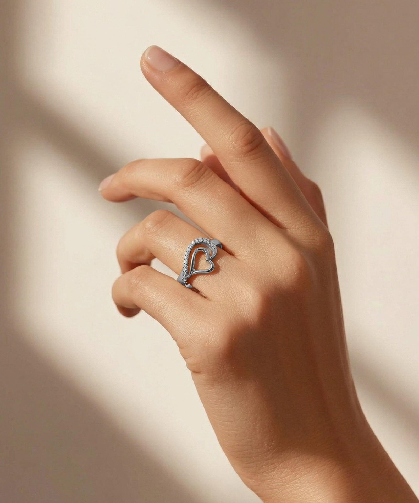 Hand wearing a silver ring with a heart design on a soft beige background
