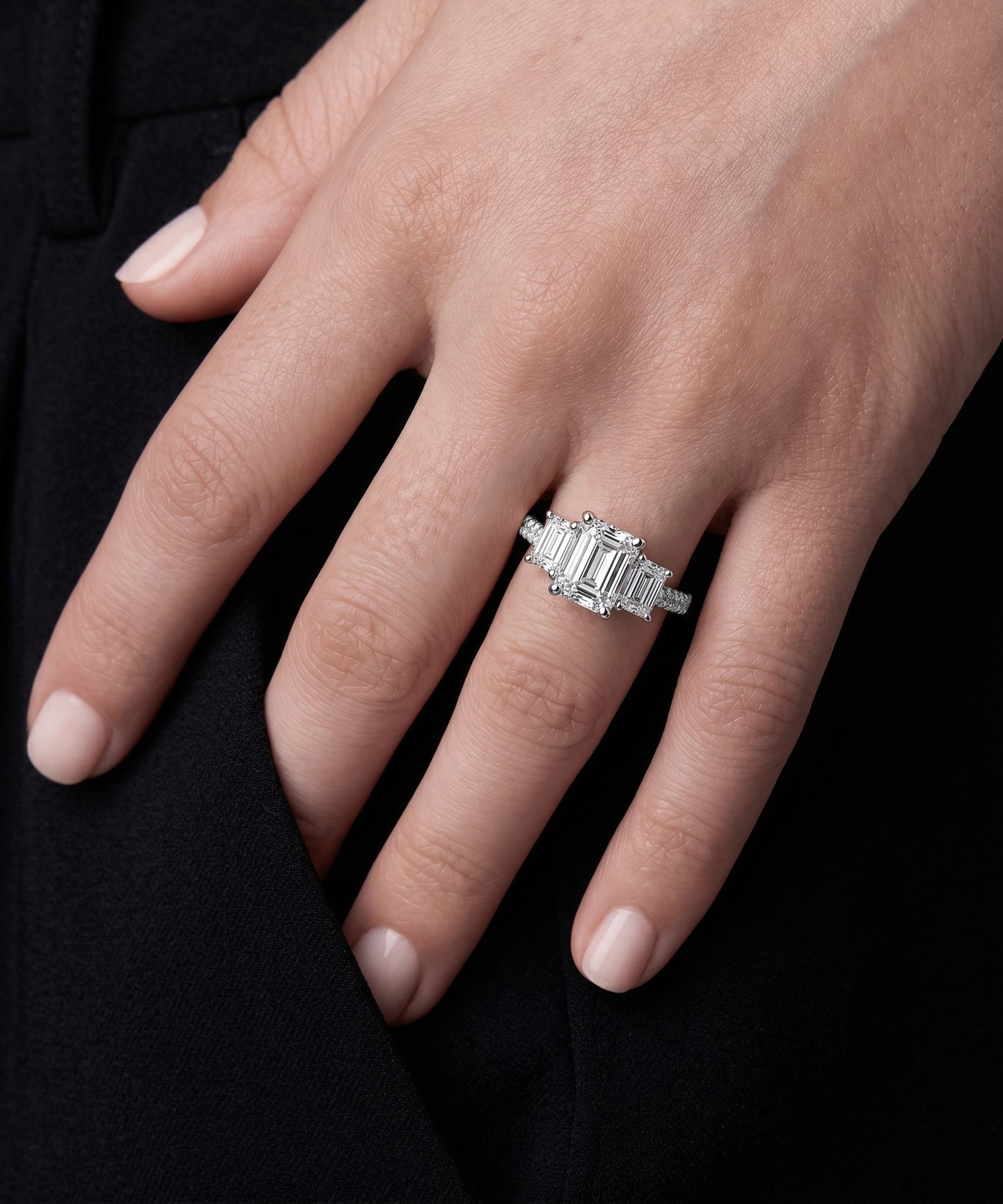 Emerald-cut diamond five-stone ring with a pavé band on a hand.
