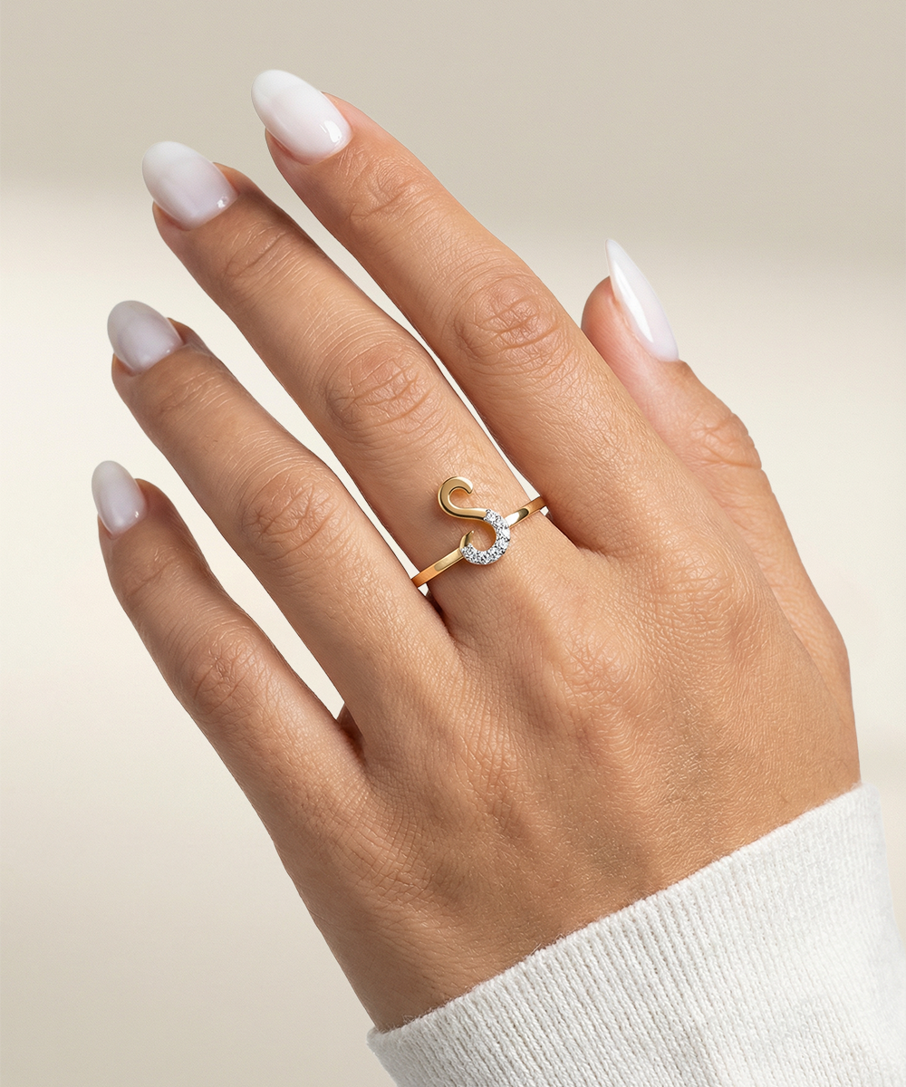 Hand wearing a gold ring with a diamond on a neutral background