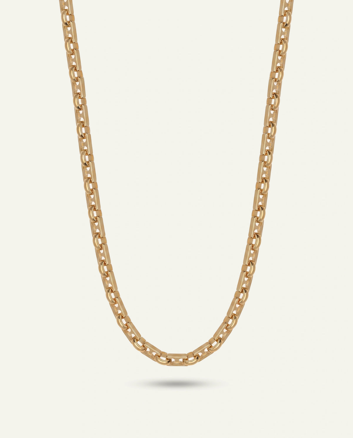 A gold-toned chain necklace with a wide, polished curb link design, shown against a solid off-white background with a soft shadow underneath.