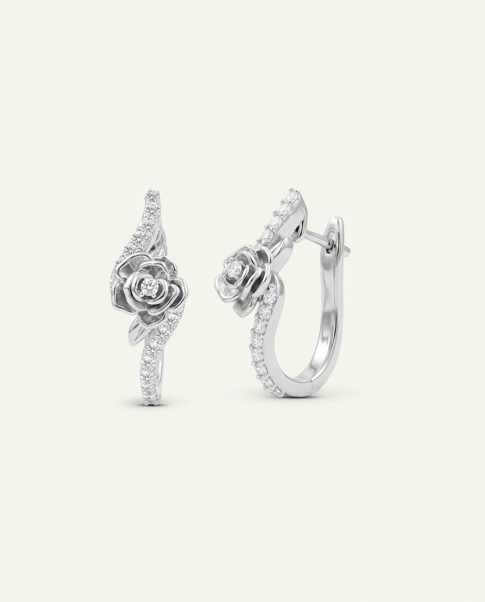 A pair of silver huggie hoop earrings featuring a detailed rose motif and pavé-set clear stones, shown on a light cream background.