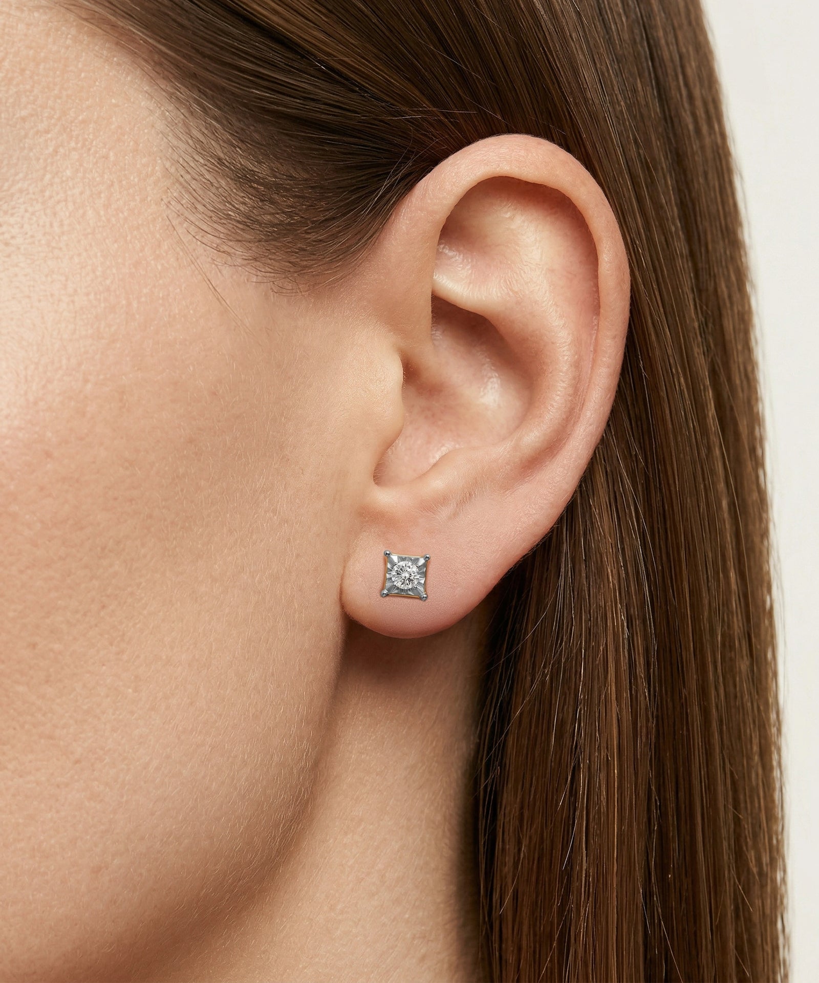 Close-up of an ear wearing a square stud earring with a clear gemstone.