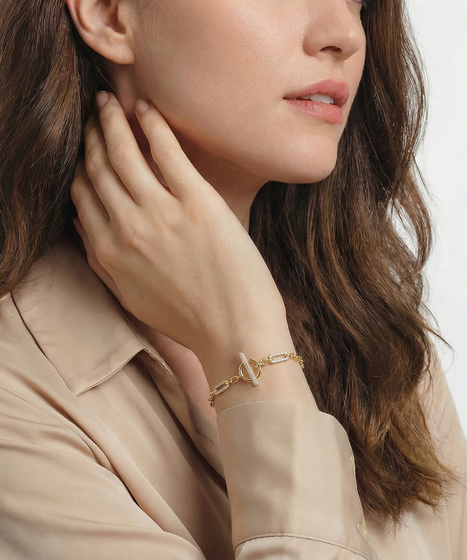 Woman wearing a gold bracelet with a subtle design, touching her face.