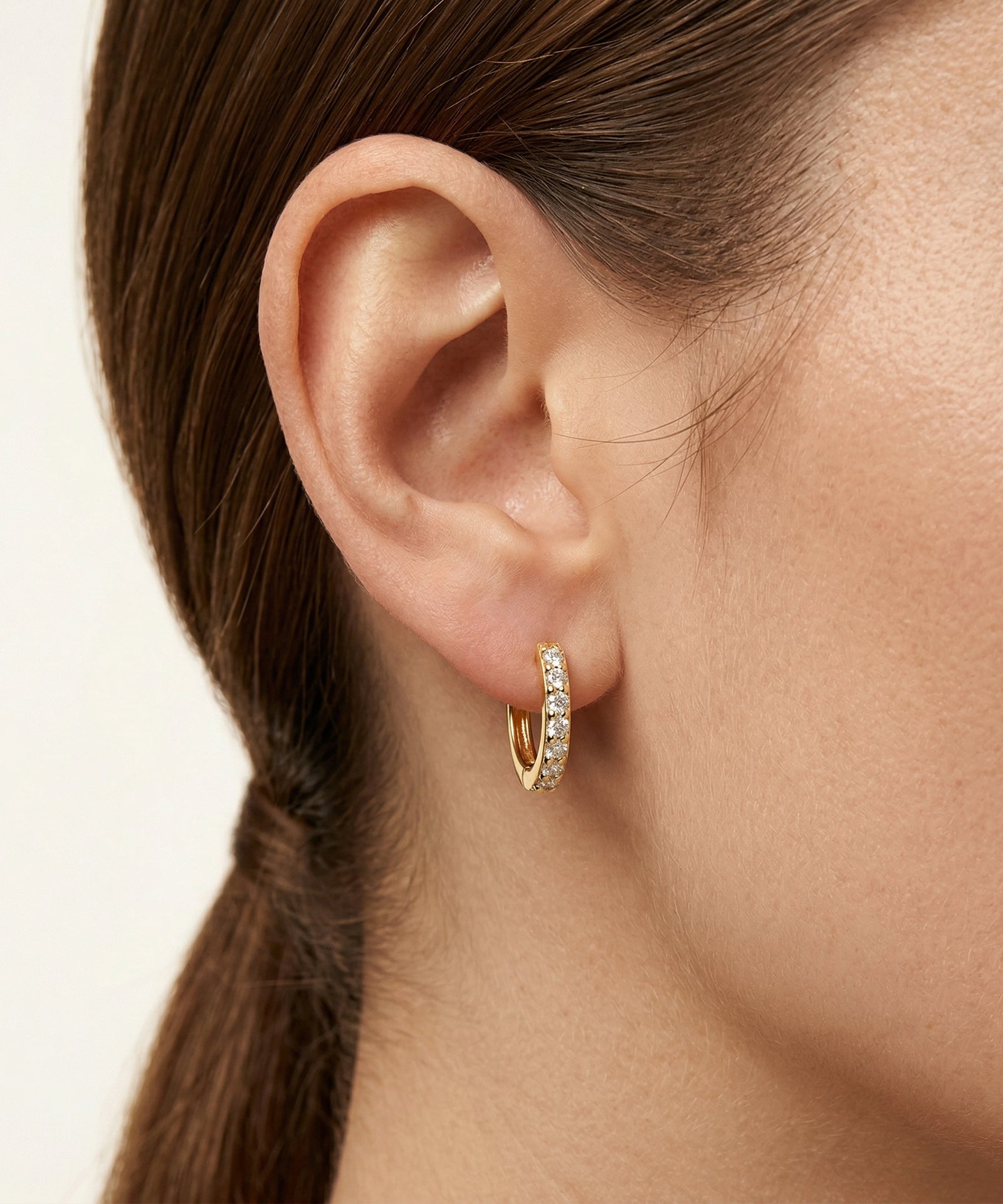 Close-up of an ear wearing a gold hoop earring with a blurred background