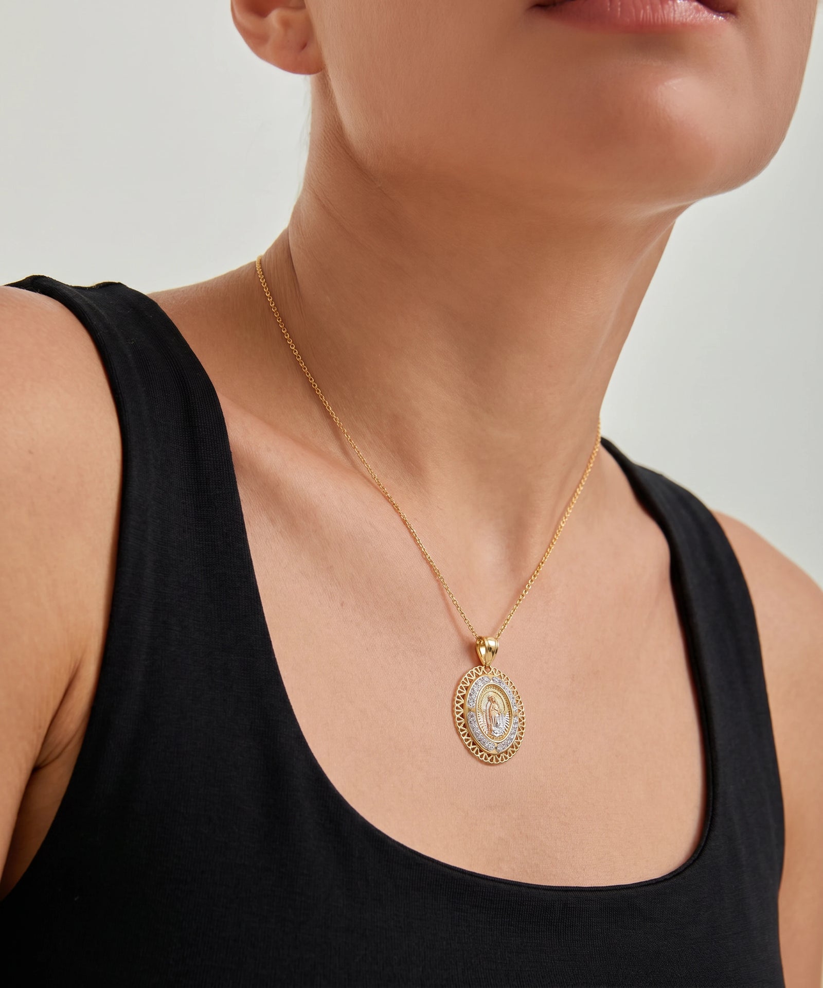 Person wearing a gold necklace with a pendant on a plain background
