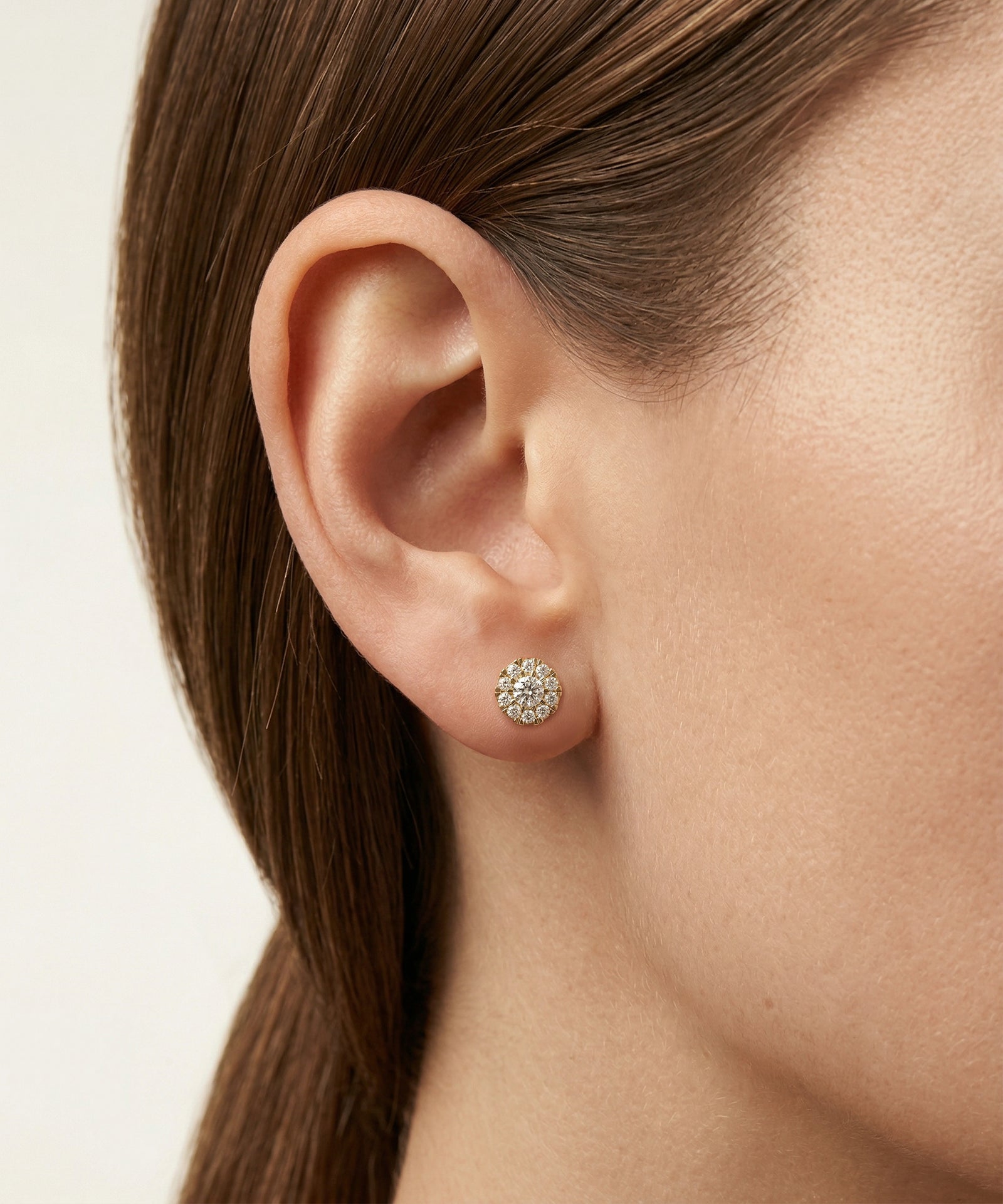 Close-up of an ear wearing a diamond stud earring on a neutral background