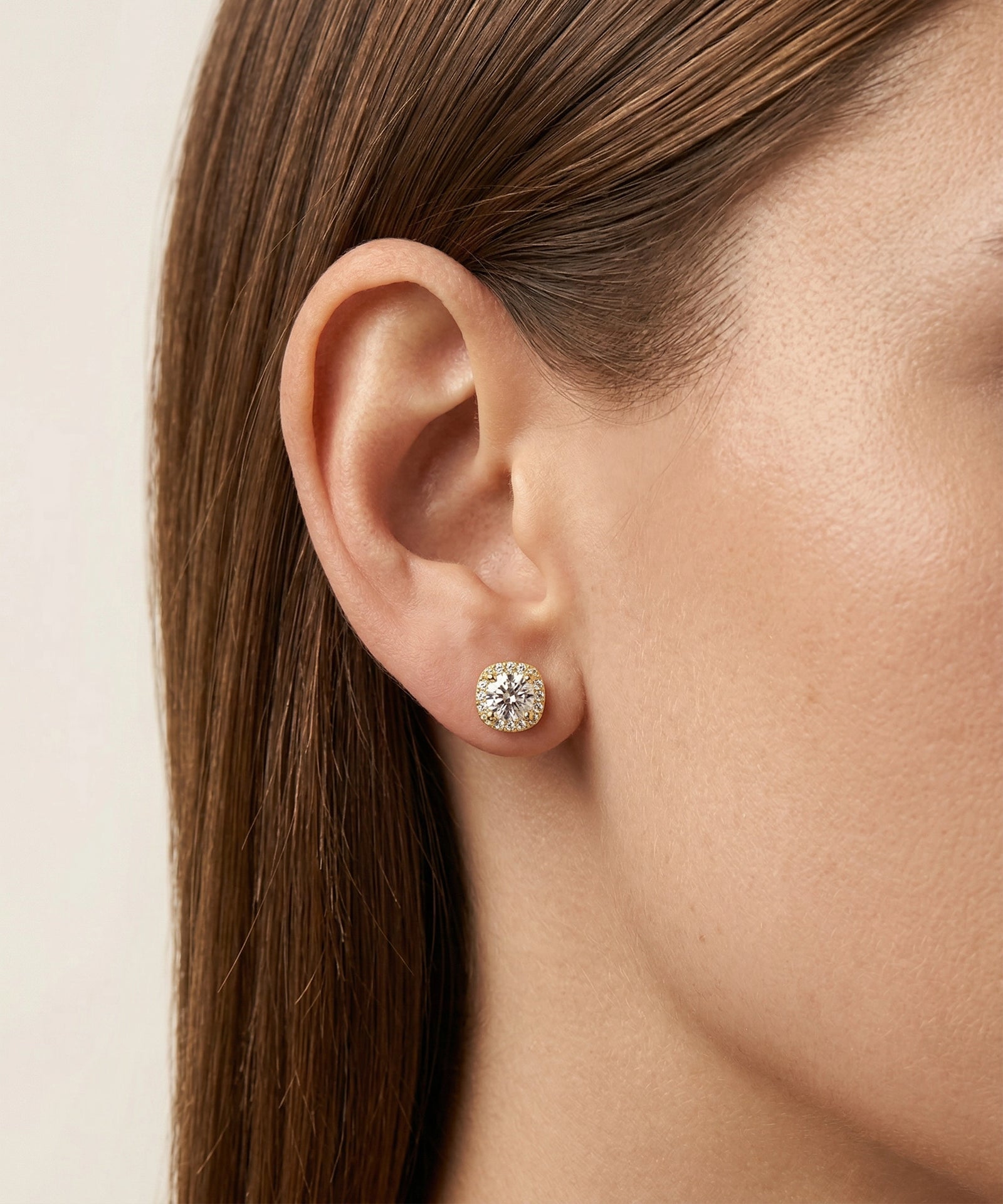 Close-up of a woman's ear wearing a diamond stud earring against a neutral background