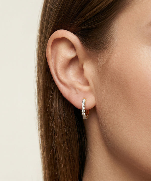 Close-up of an ear wearing a silver hoop earring on a neutral background
