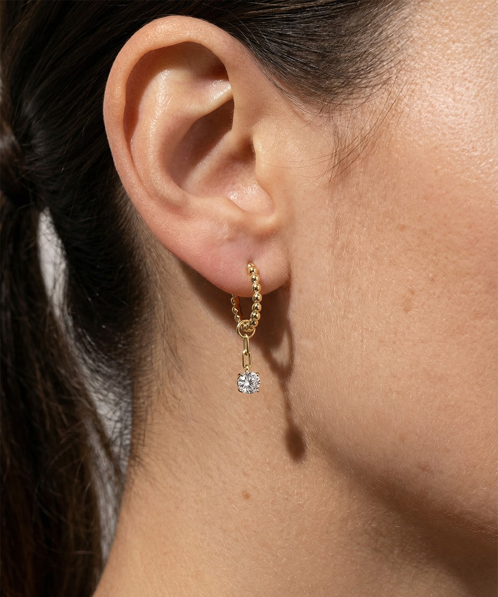 Close-up of an ear wearing a gold earring with a diamond pendant.
