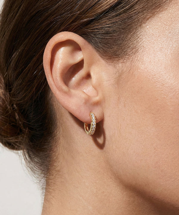 Close-up of an ear wearing a gold hoop earring with a blurred background