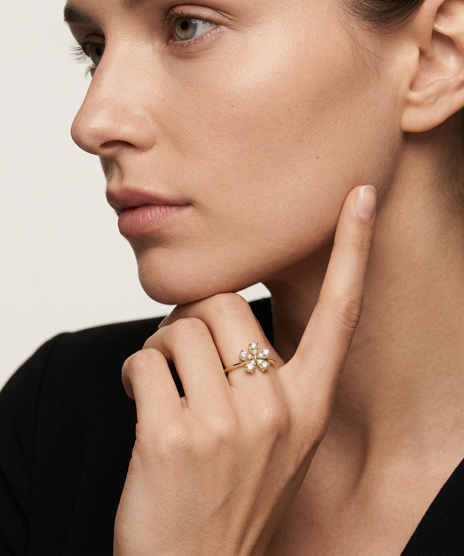 Close-up of a woman wearing a gold ring with a floral design on a neutral background