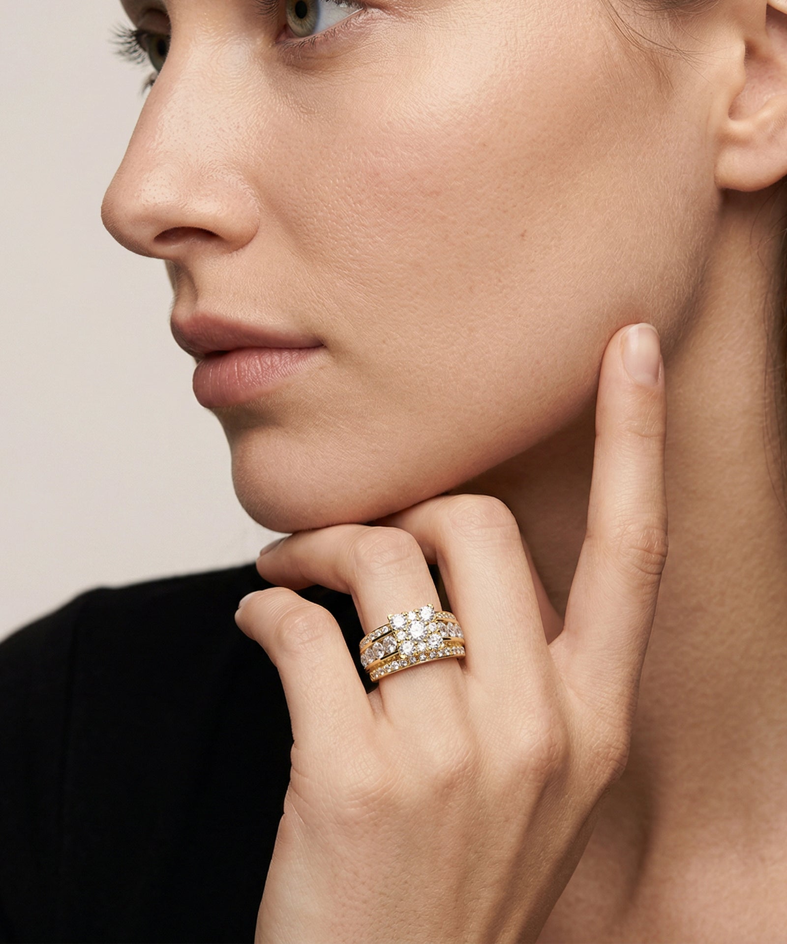 Close-up of a woman's face wearing a diamond ring on her finger against a neutral background
