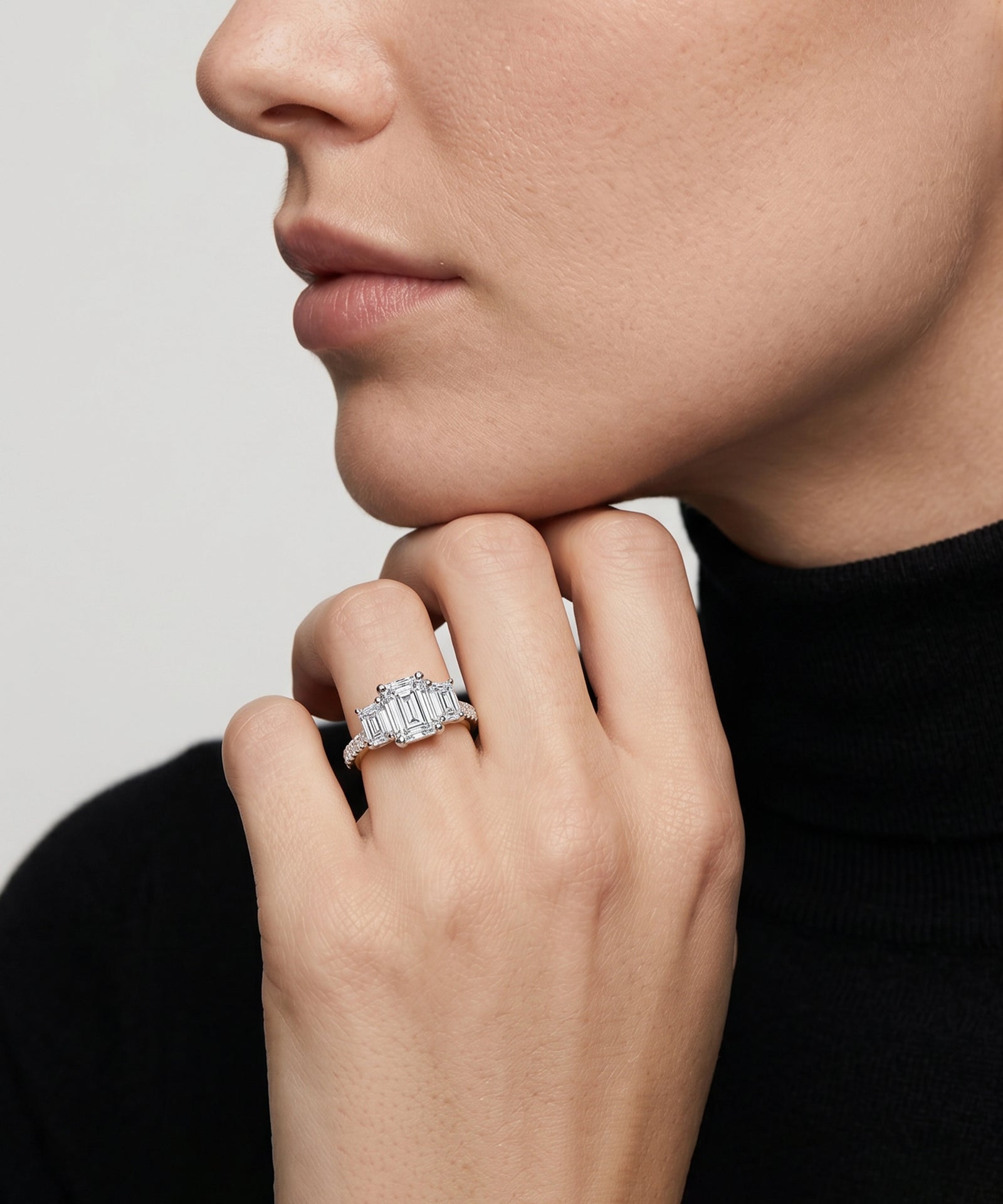 Emerald-cut diamond five-stone ring with a pavé band on a model's hand.