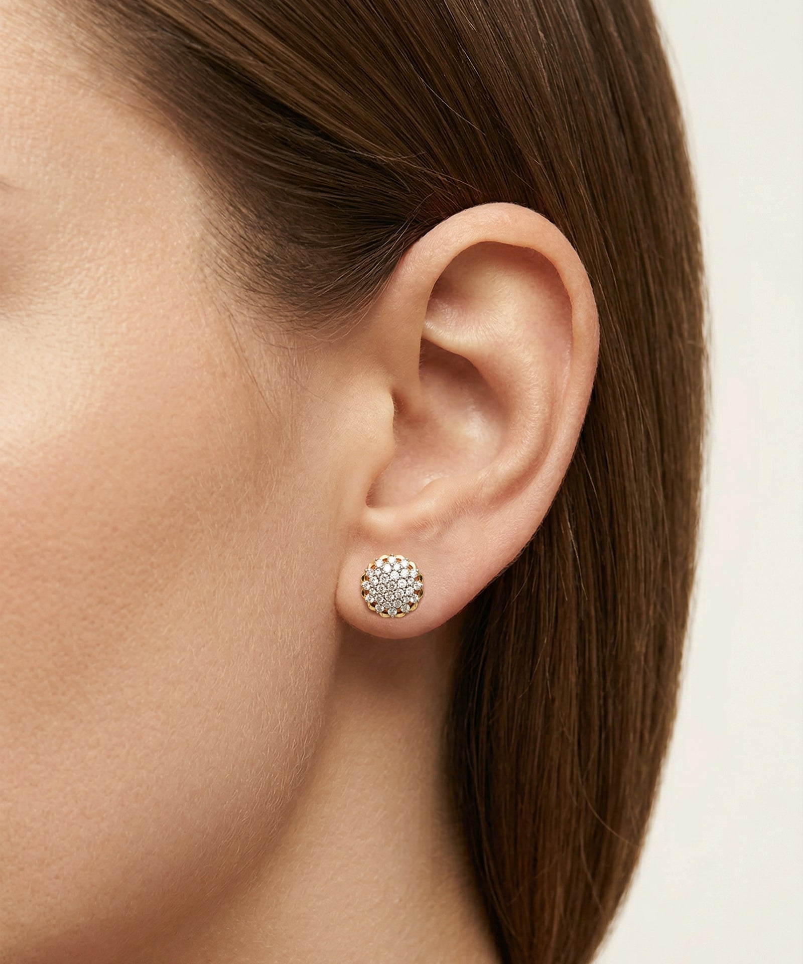 Close-up of an ear wearing a diamond stud earring with a neutral background