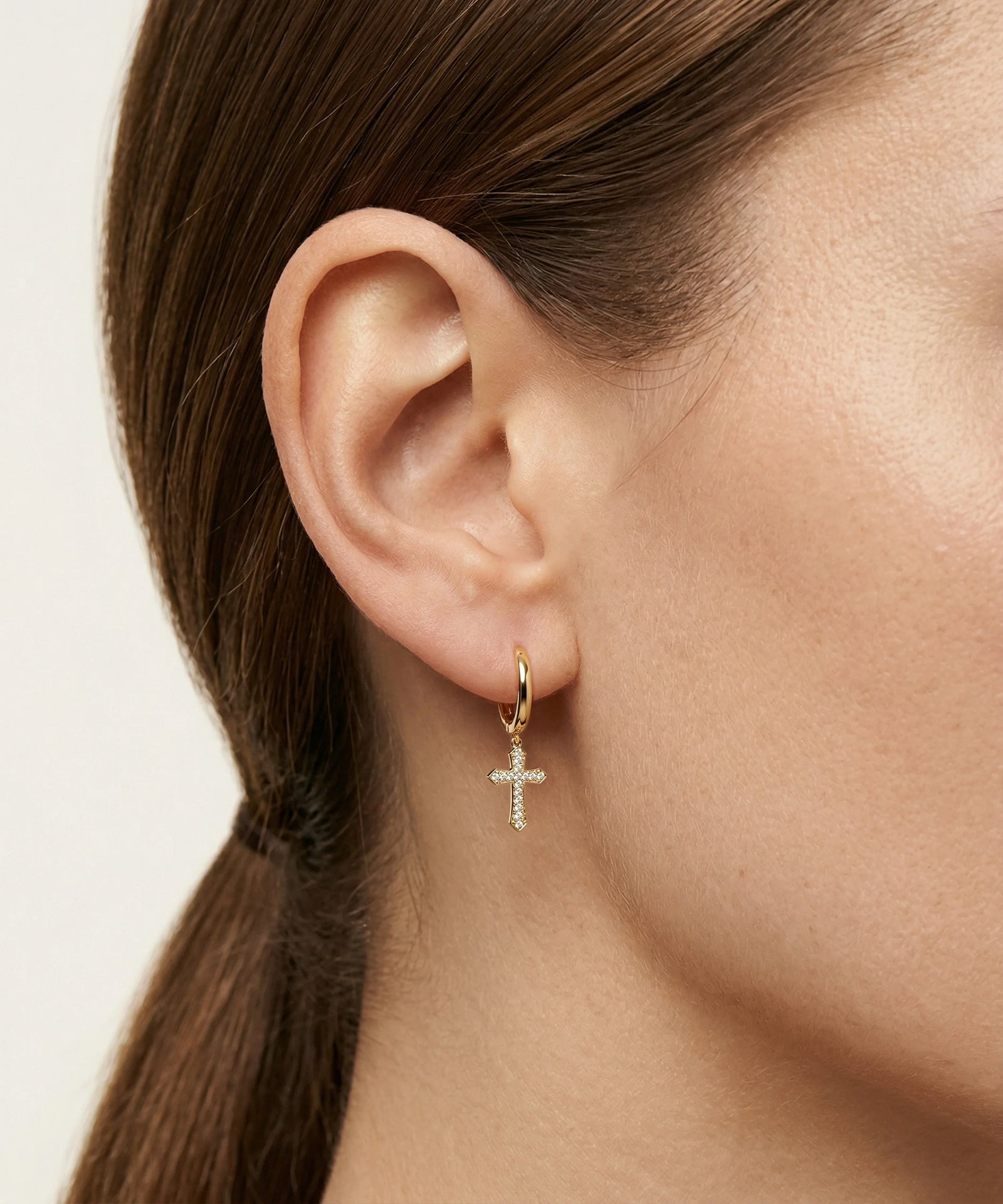 Gold cross earring worn by a person with a neutral background