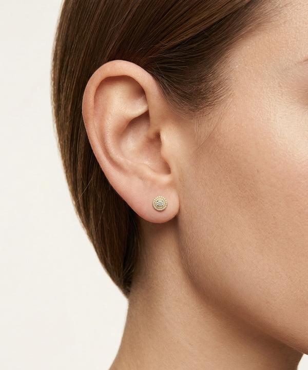 Close-up of an ear wearing a small round earring on a neutral background