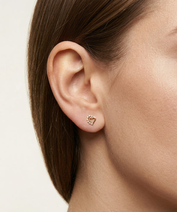 Close-up of an ear wearing a heart-shaped earring on a neutral background