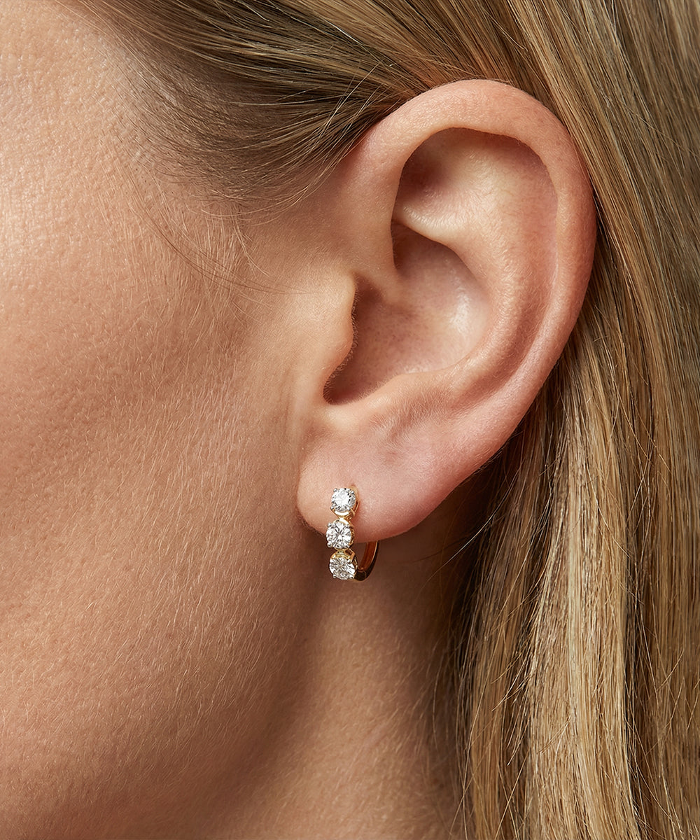 Close-up of an ear wearing a diamond hoop earring with blonde hair.