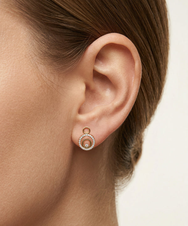 Close-up of an ear wearing a rose gold earring with a pearl center on a neutral background