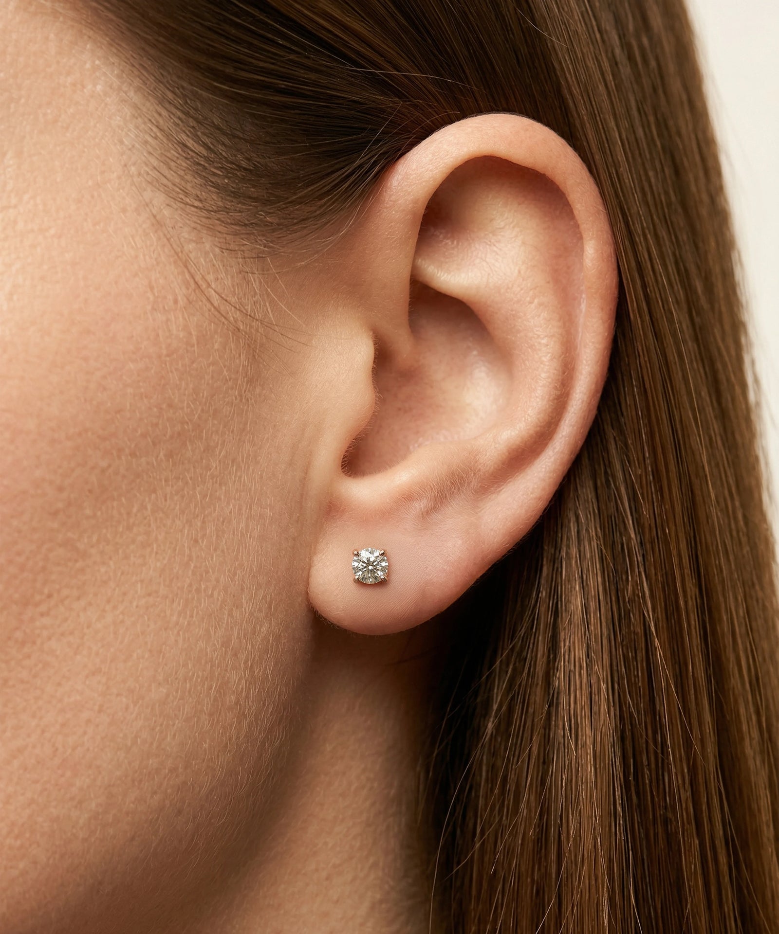 Close-up of an ear wearing a diamond stud earring with hair partially obscuring the view.
