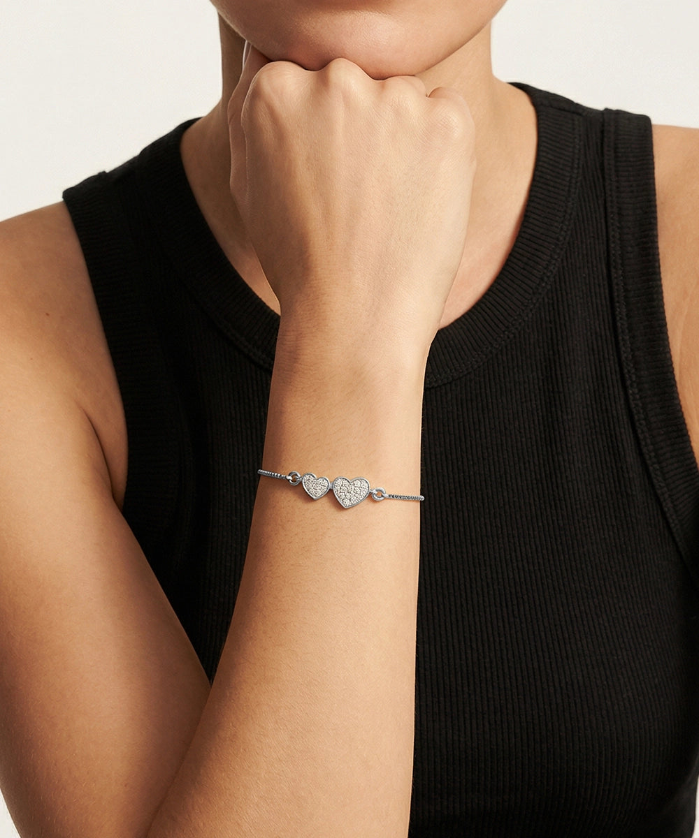Person wearing a silver bracelet with heart charms on a plain background