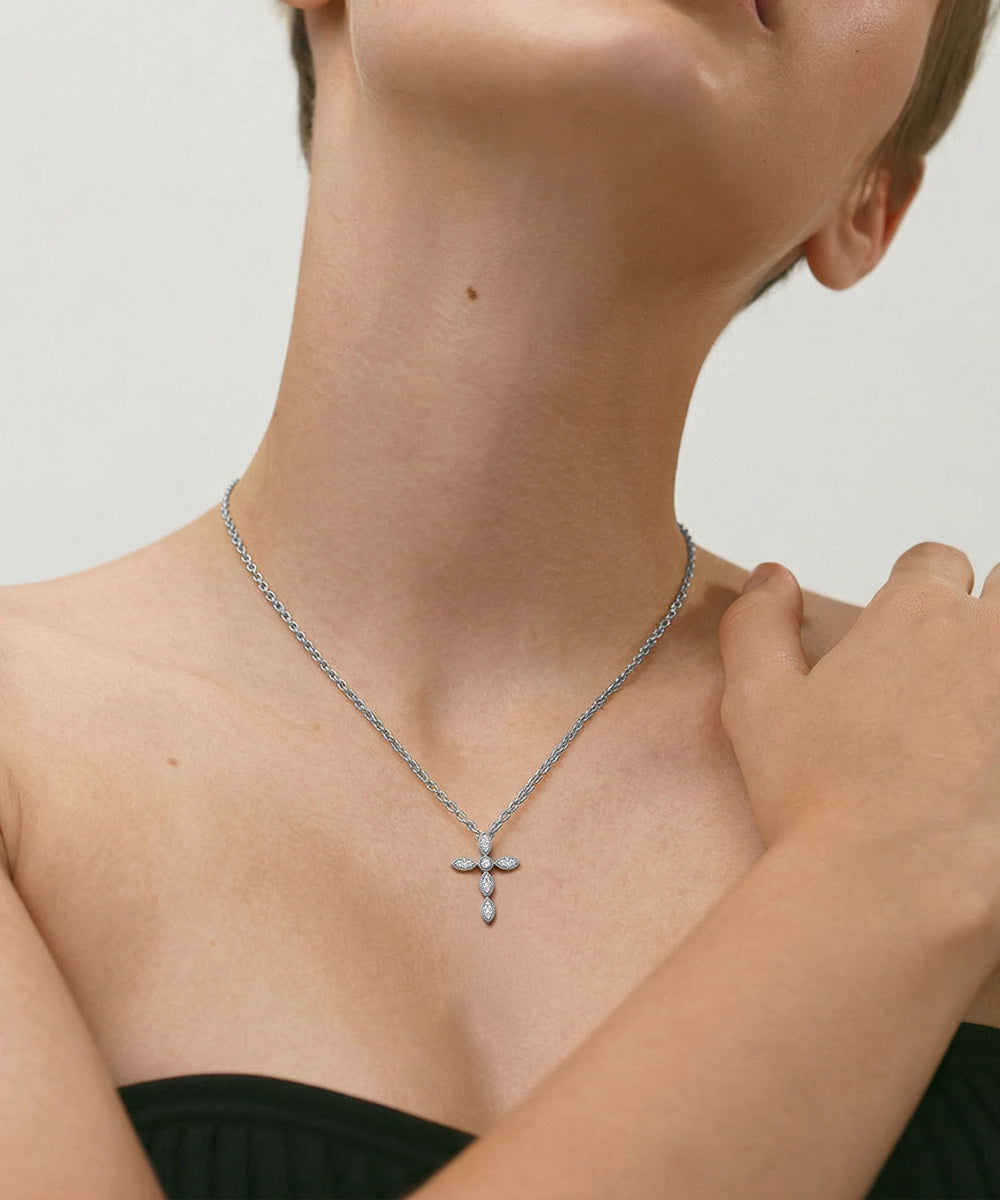 Person wearing a silver necklace with a cross pendant on a neutral background