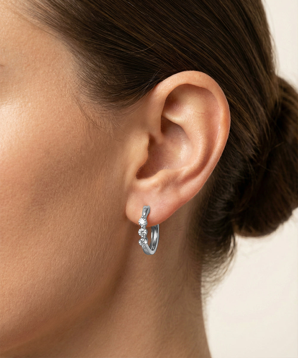 Close-up of an ear wearing a silver earring with a clear gemstone.