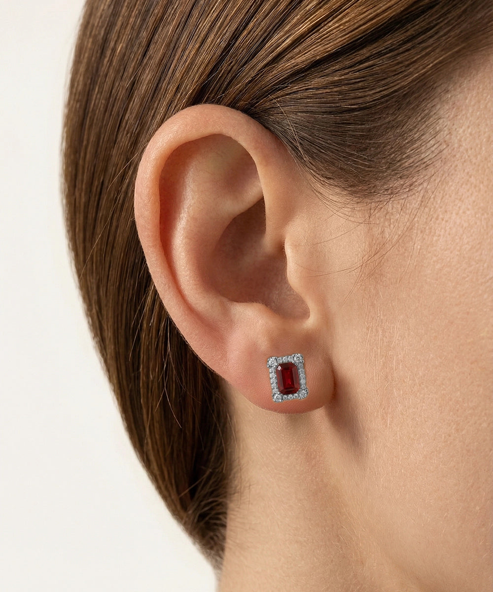 Close-up of an ear wearing a red gemstone earring with a silver setting.