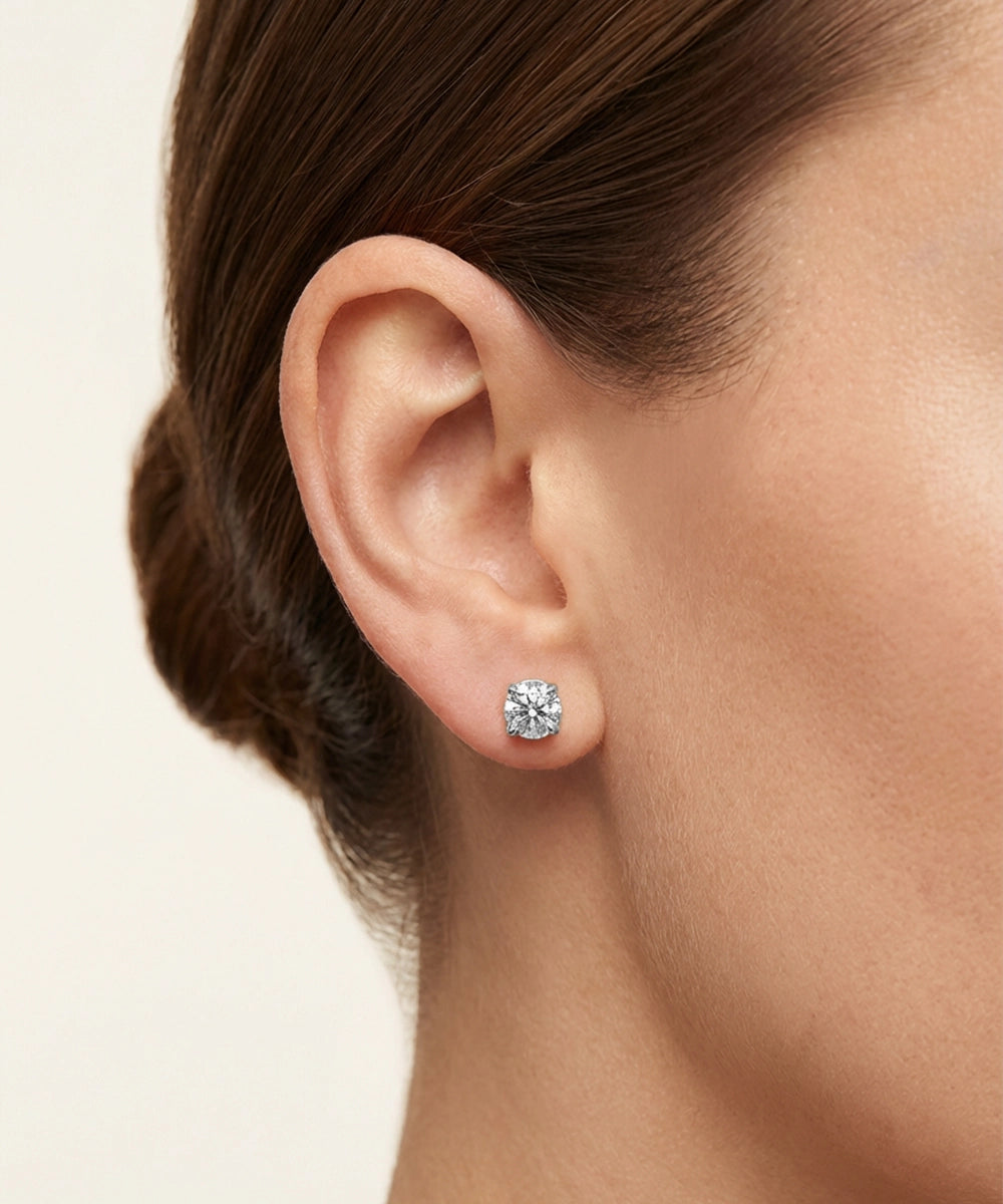 Close-up of an ear wearing a diamond stud earring on a neutral background
