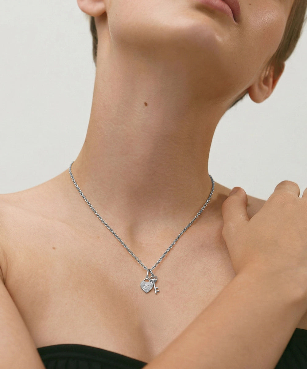 Person wearing a silver necklace with heart and key charms on a neutral background