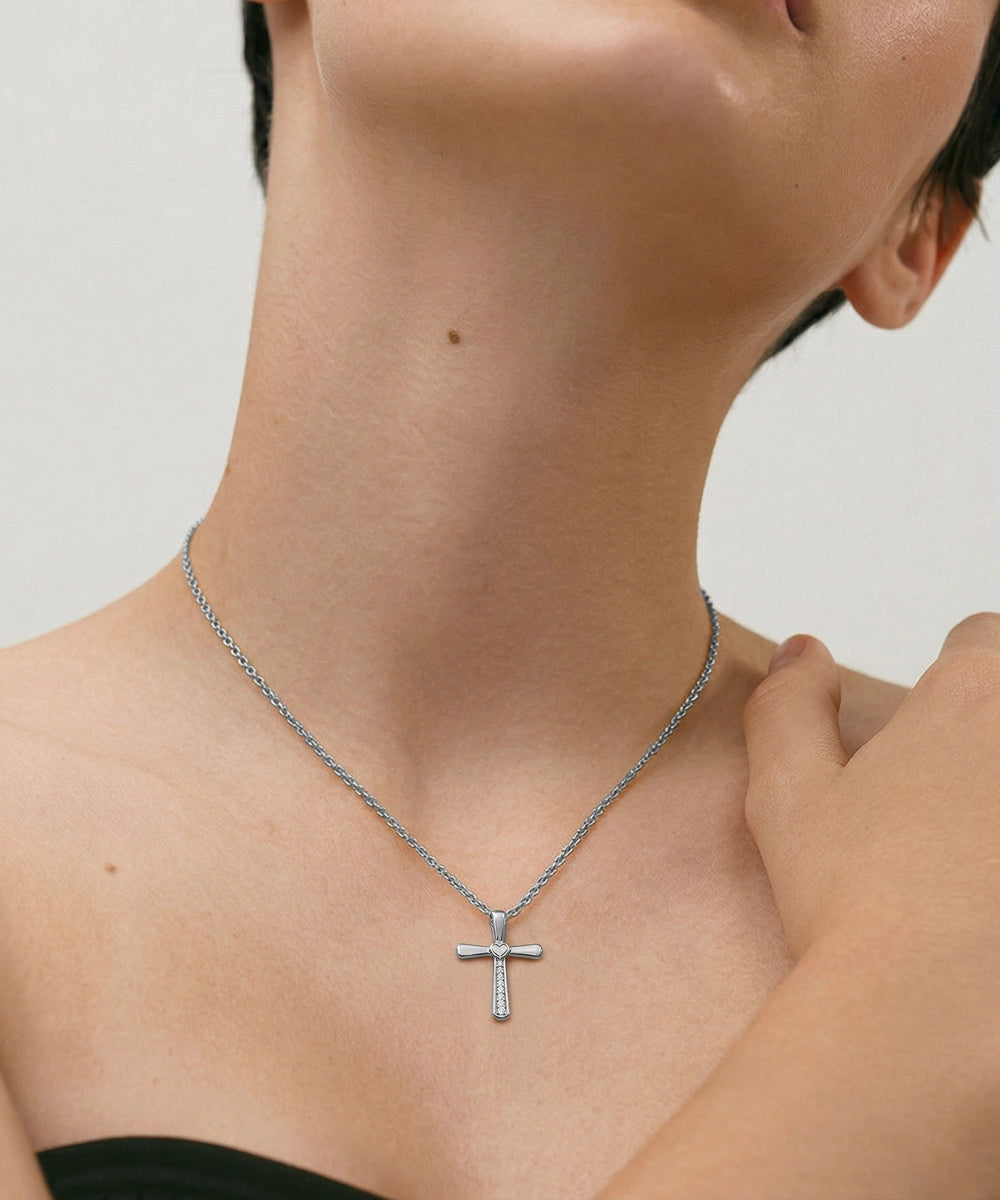 Person wearing a silver cross necklace on a neutral background