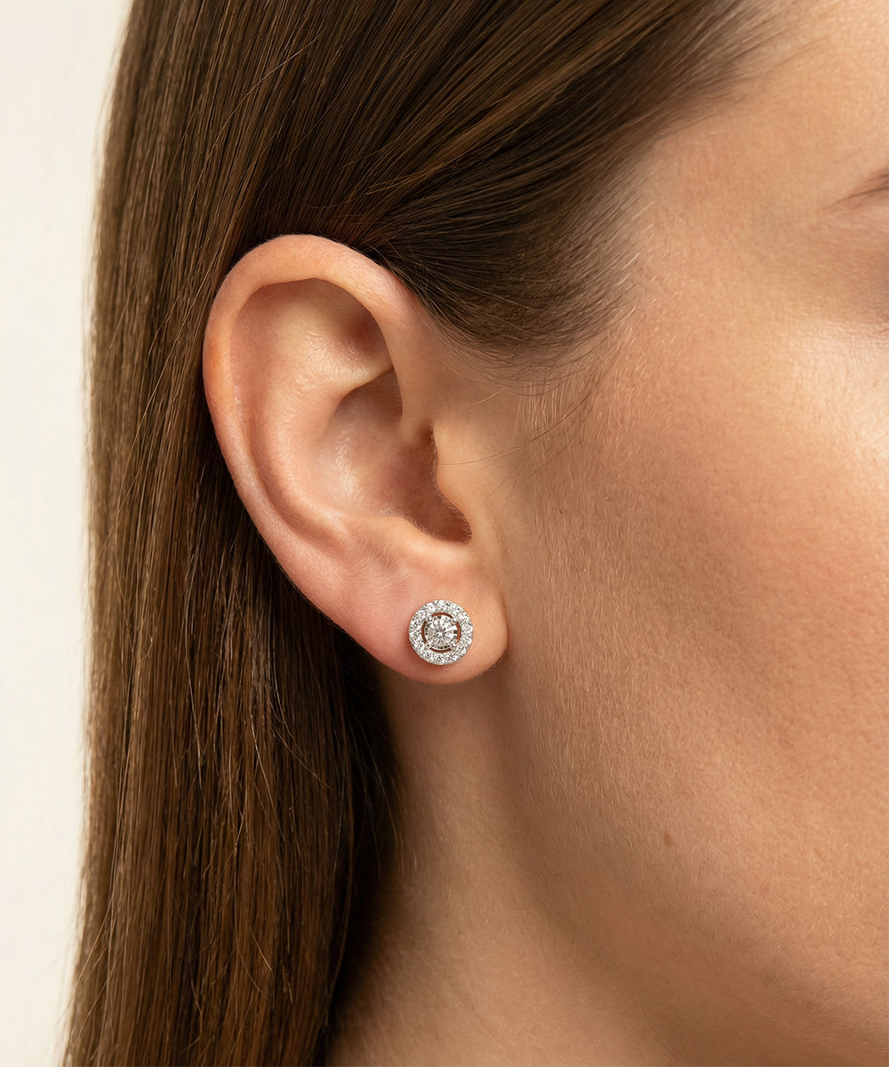 Close-up of an ear wearing a diamond stud earring on a neutral background