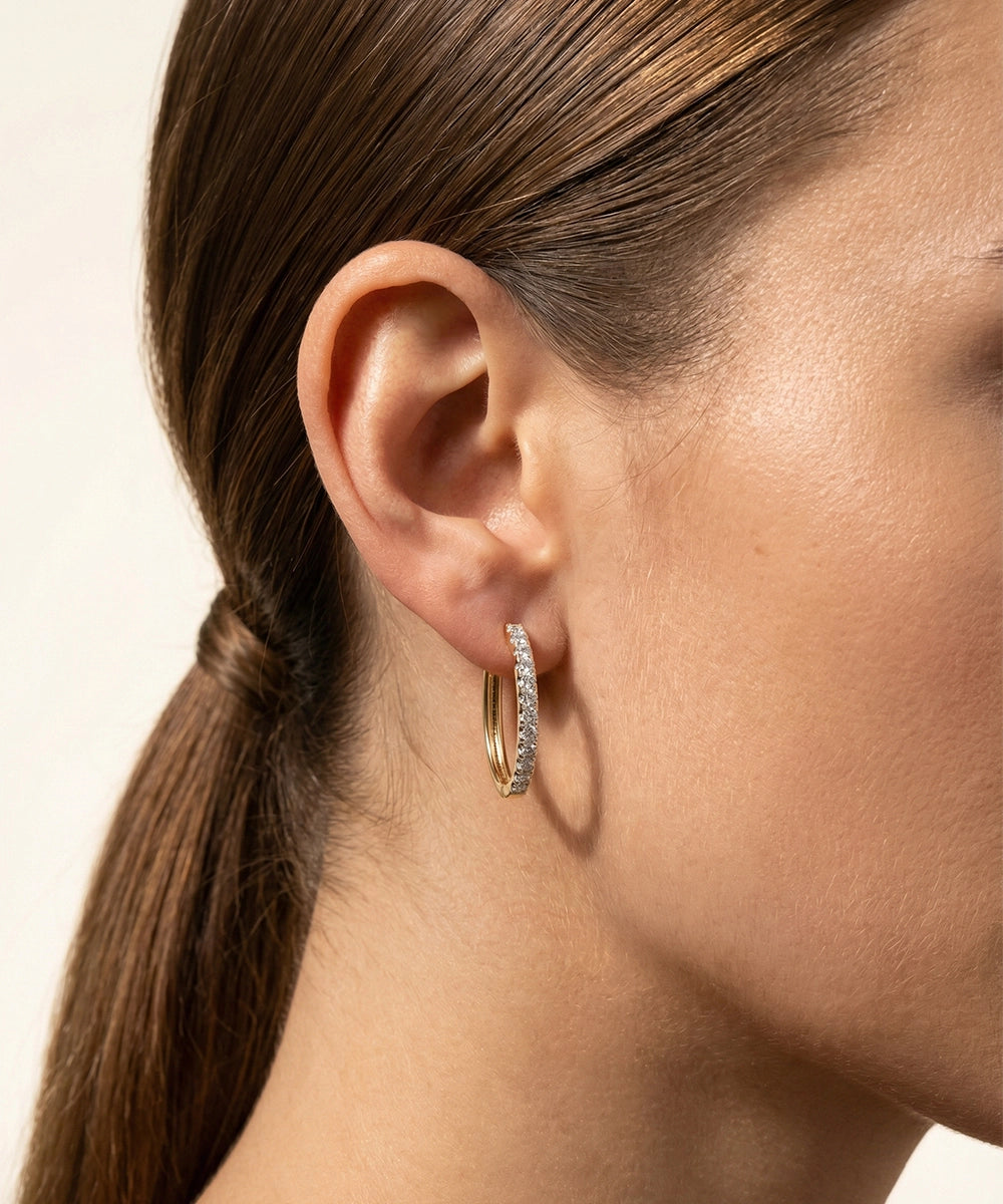 Close-up of a person wearing gold hoop earrings with a neutral background