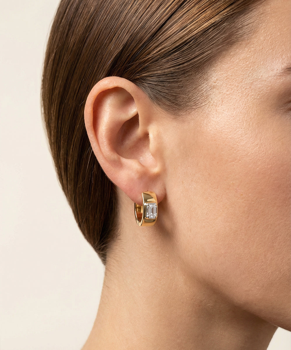 Gold hoop earrings with a diamond on a neutral background