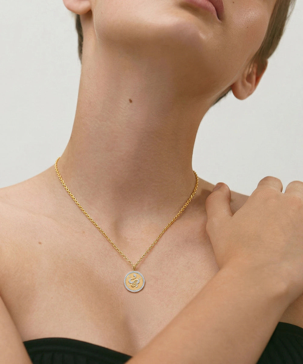 Woman wearing a gold necklace with a circular pendant on a neutral background