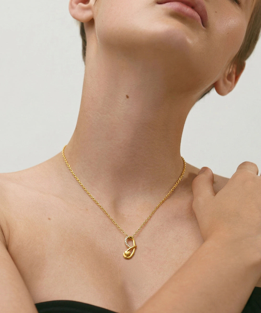 Gold necklace with a pendant on a person against a neutral background