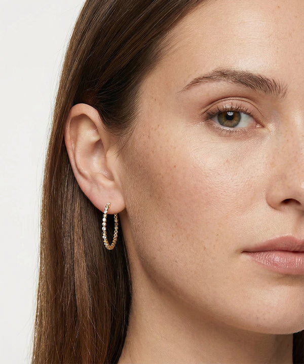 Close-up of a woman wearing gold hoop earrings with a plain background