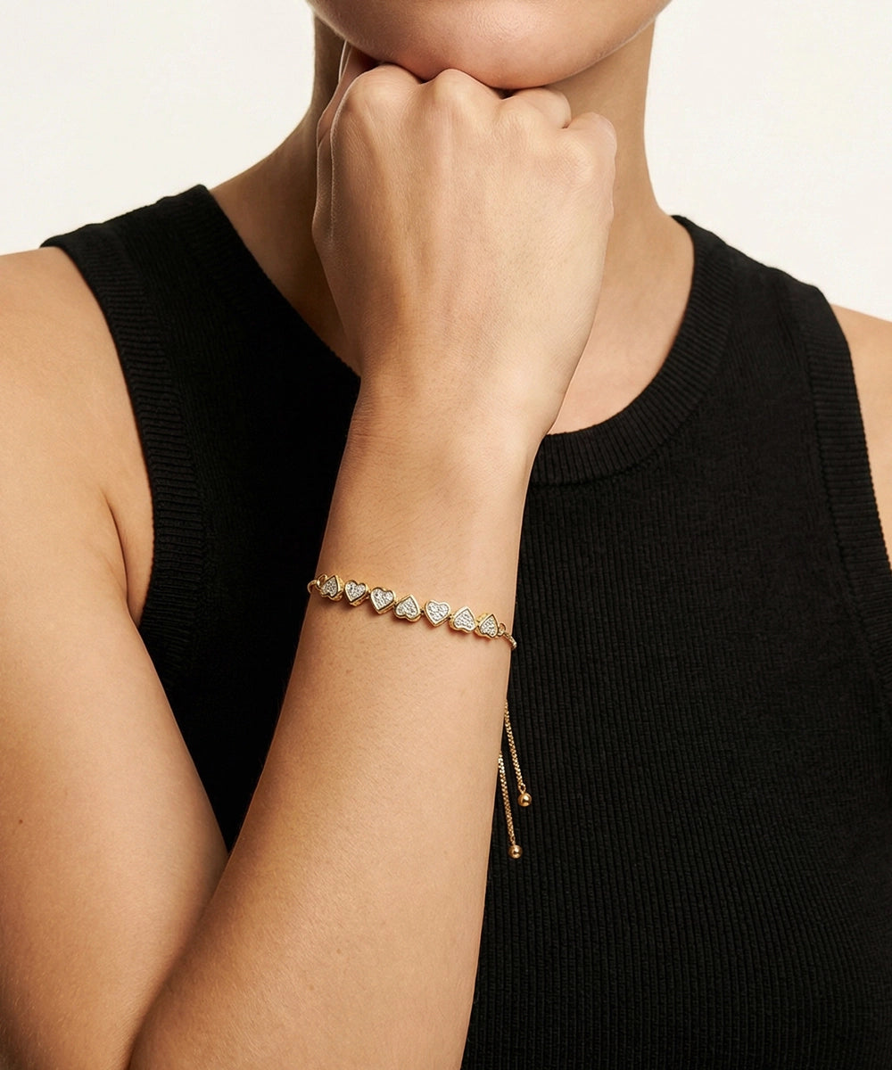 Person wearing a gold bracelet with heart-shaped charms on a plain background