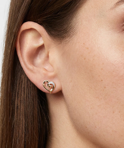 Close-up of a person wearing a gold heart-shaped earring. - alternate view