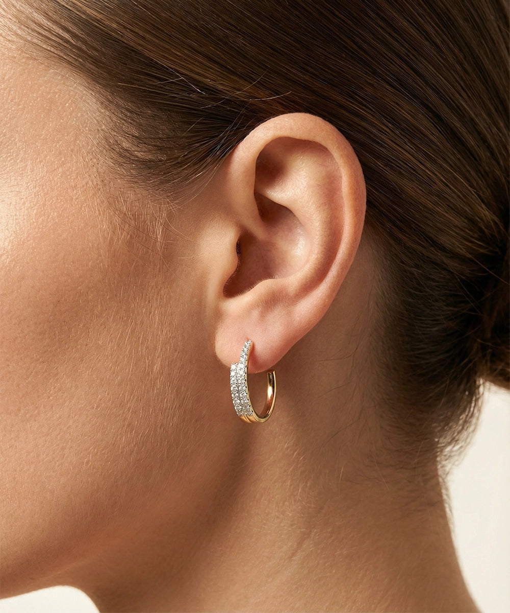 Close-up of an ear wearing a gold hoop earring with clear stones.